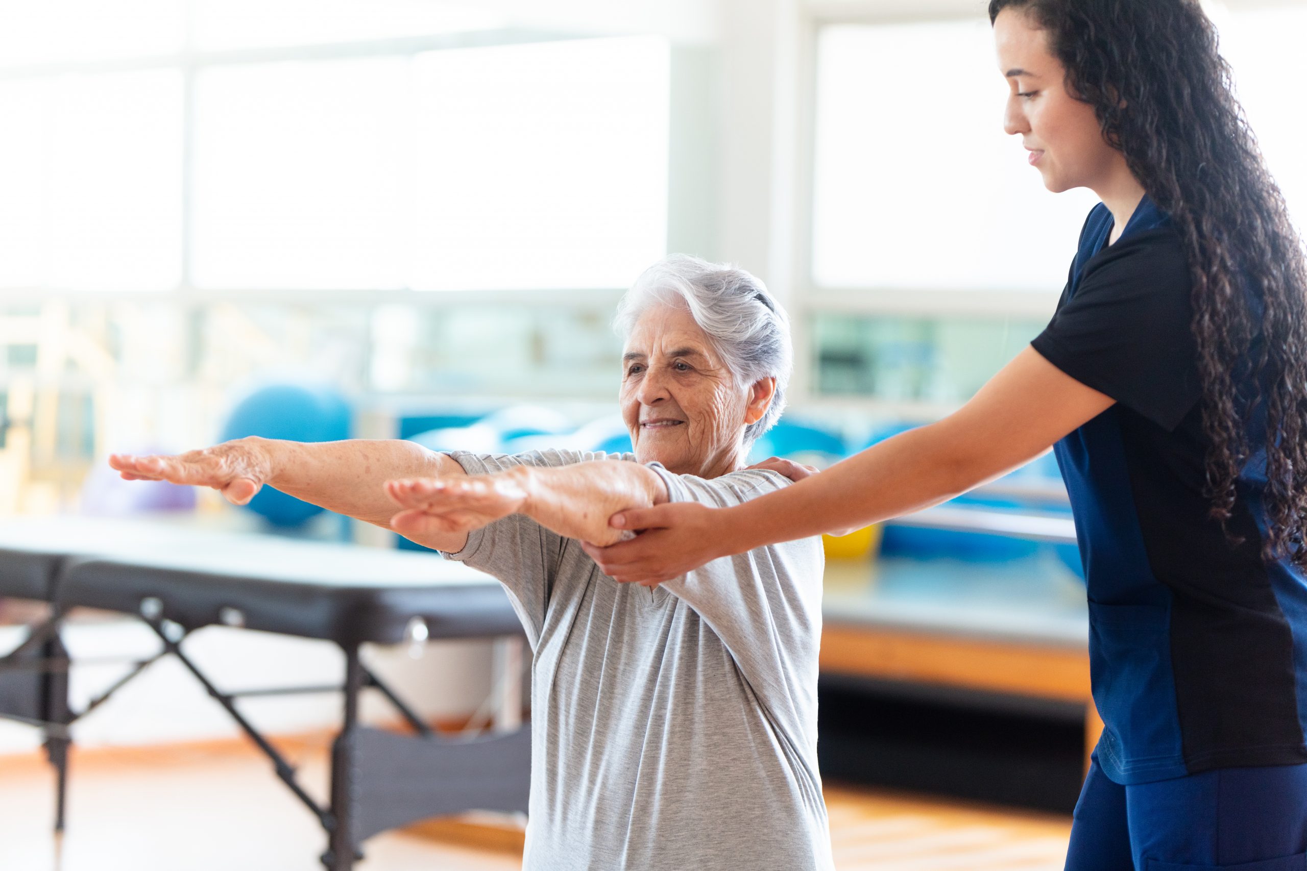 Senior woman raising arms next to a physical therapist