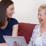 Plena Speech Pathologist, Bernadette Dutton, holding an iPad while smiling and laughing with an older female client