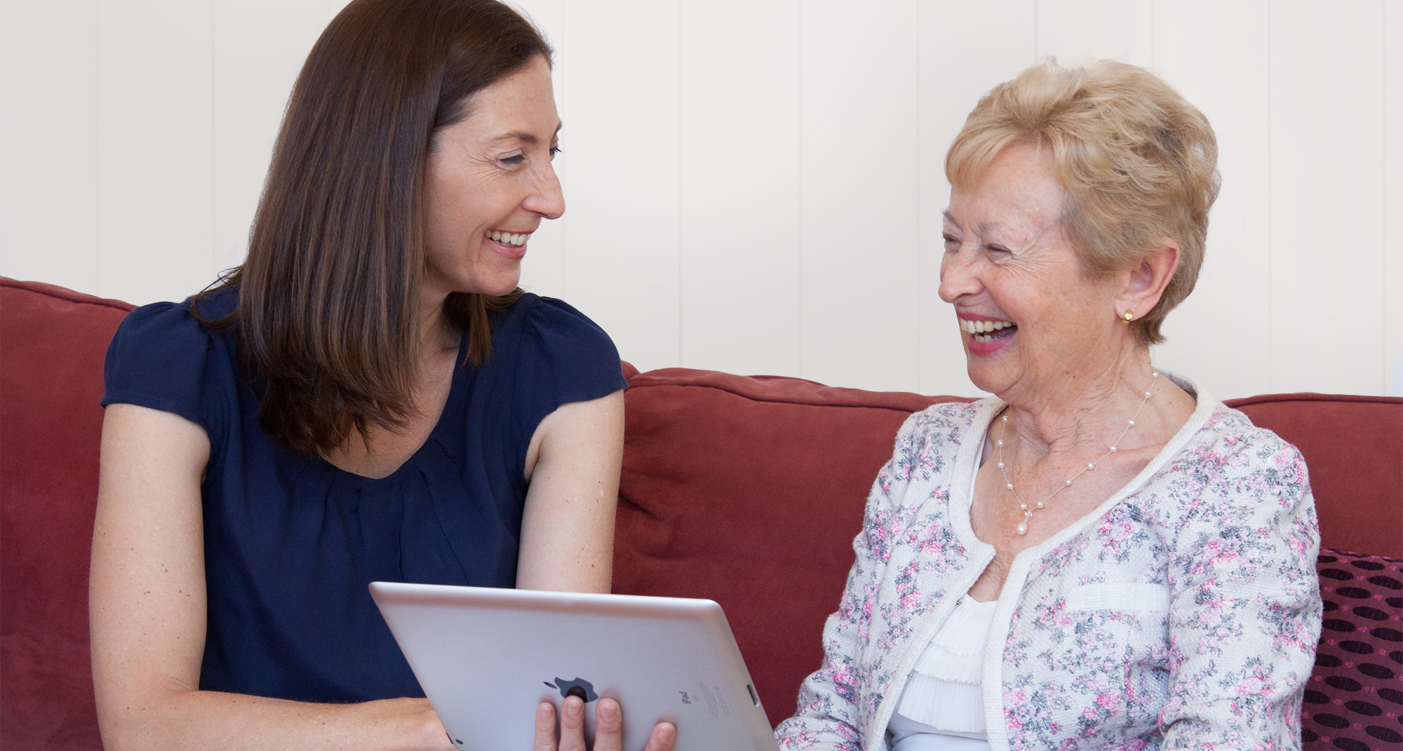 Plena Speech Pathologist, Bernadette Dutton, holding an iPad while smiling and laughing with an older female client