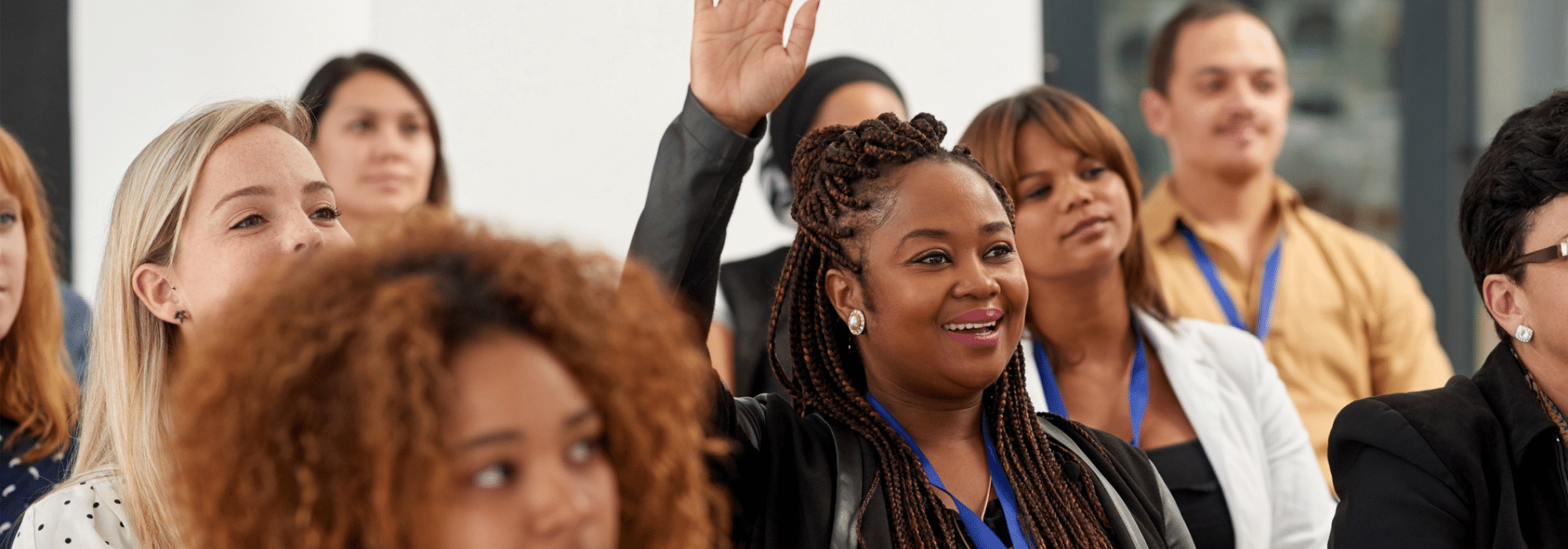 A woman sitting in a crowd of people smiling and raising her hand