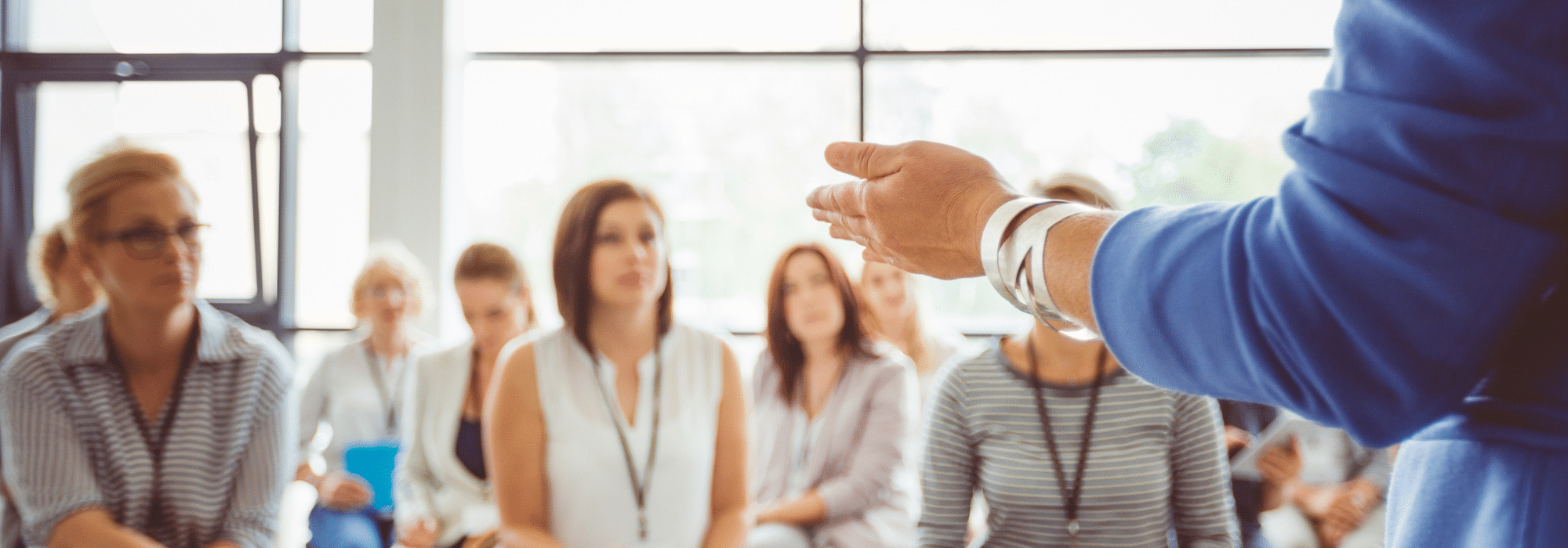 A person in blue holding out her hand to a group of people listening to her