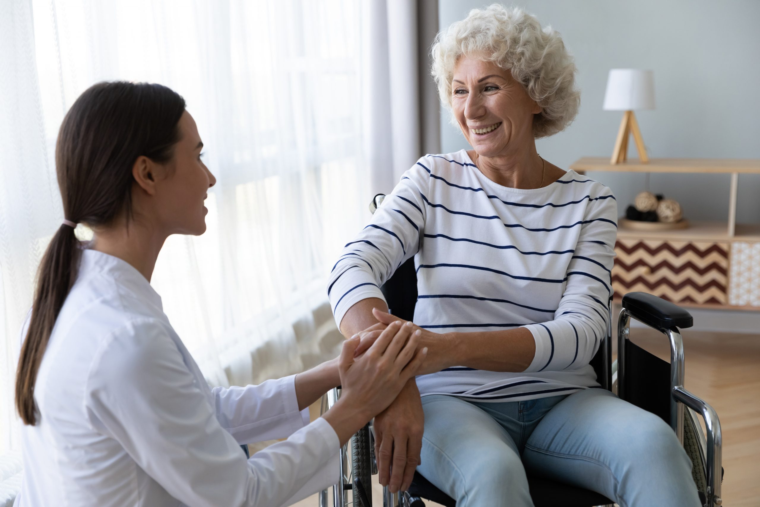 A doctor smiling and holding the arm of an older woman in a wheelchair smiling