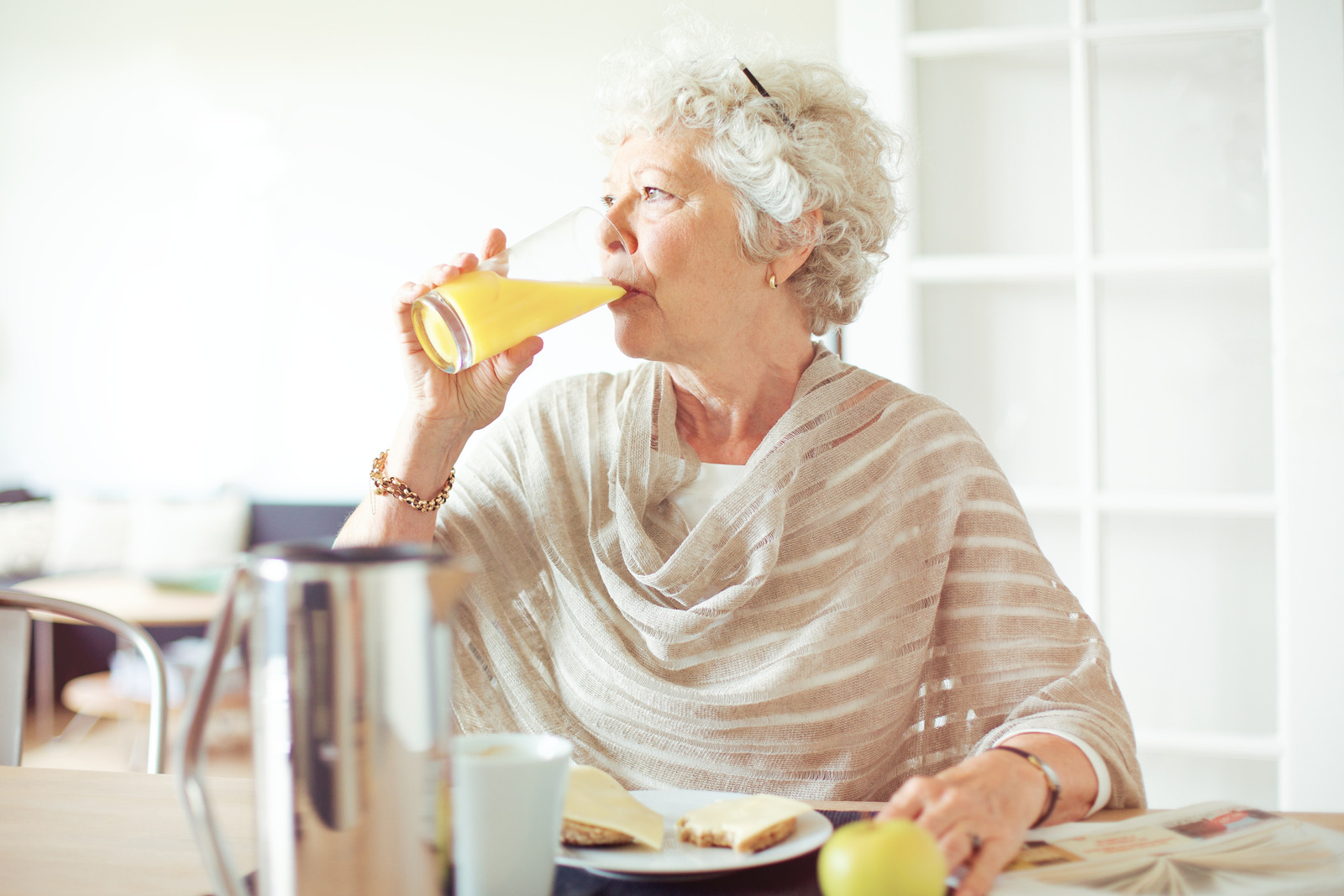 An older woman looking off camera while drinking a glass of orange juice