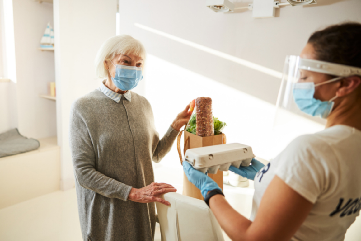 A Dietitian wearing PPE giving a tray of eggs to an older woman wearing a mask