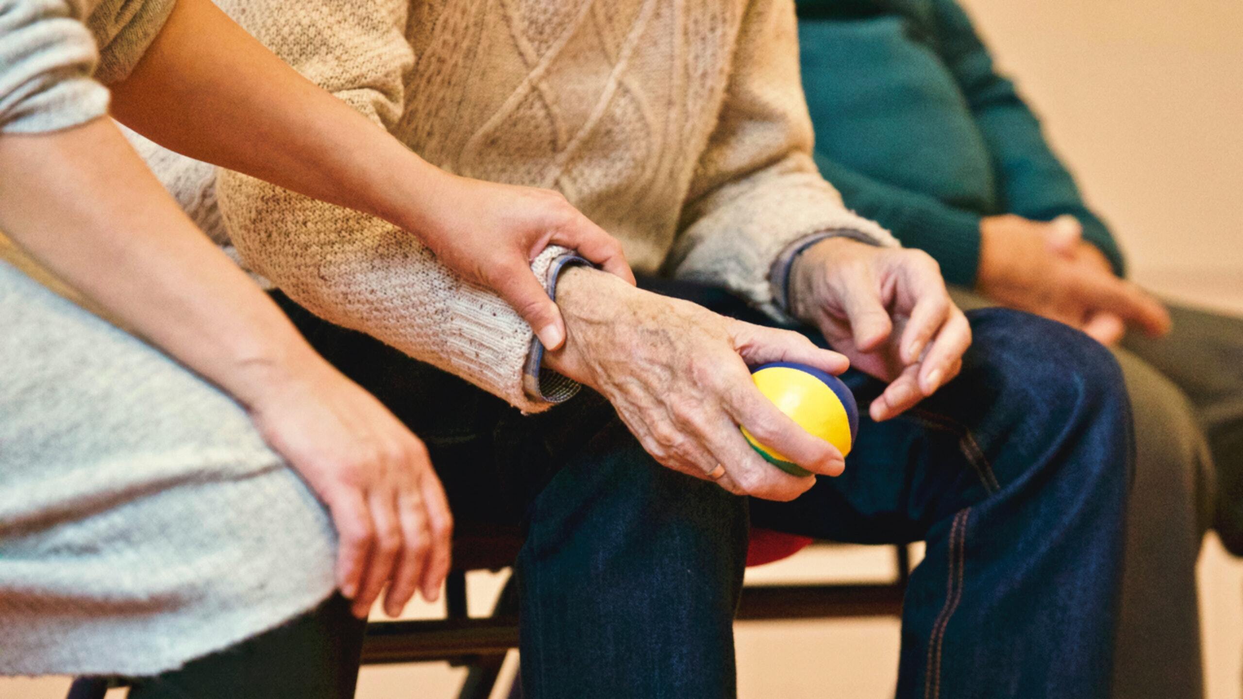 A hand holding on to the arm of an older person who is holding a ball