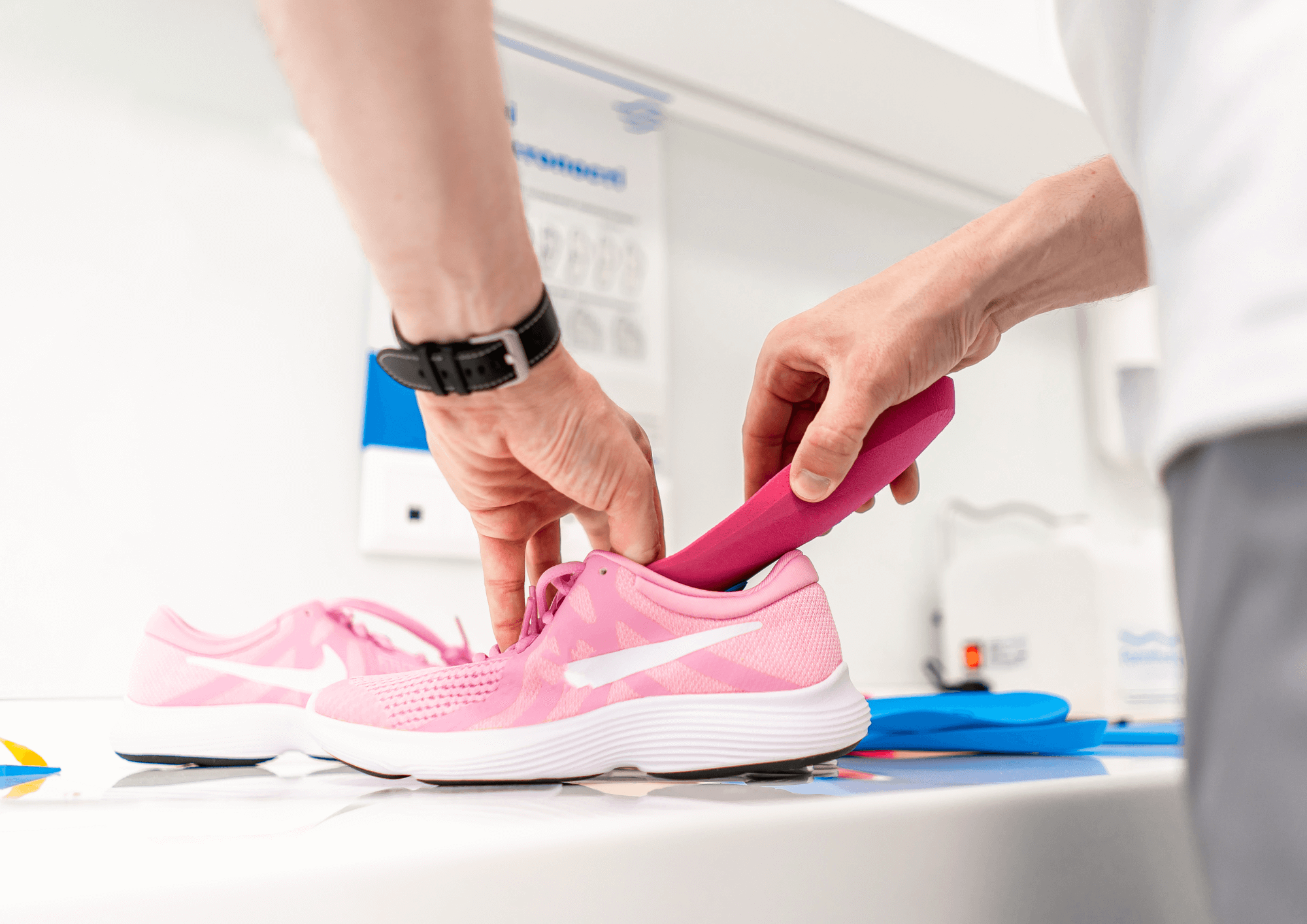A person is inserting a pink orthotic into a pink sneaker.