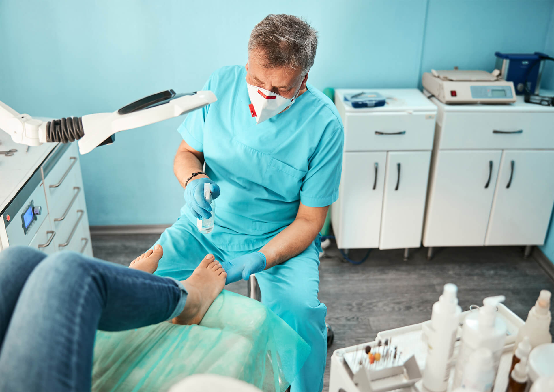 A white male Podiatrist sits treating the feet of a person.