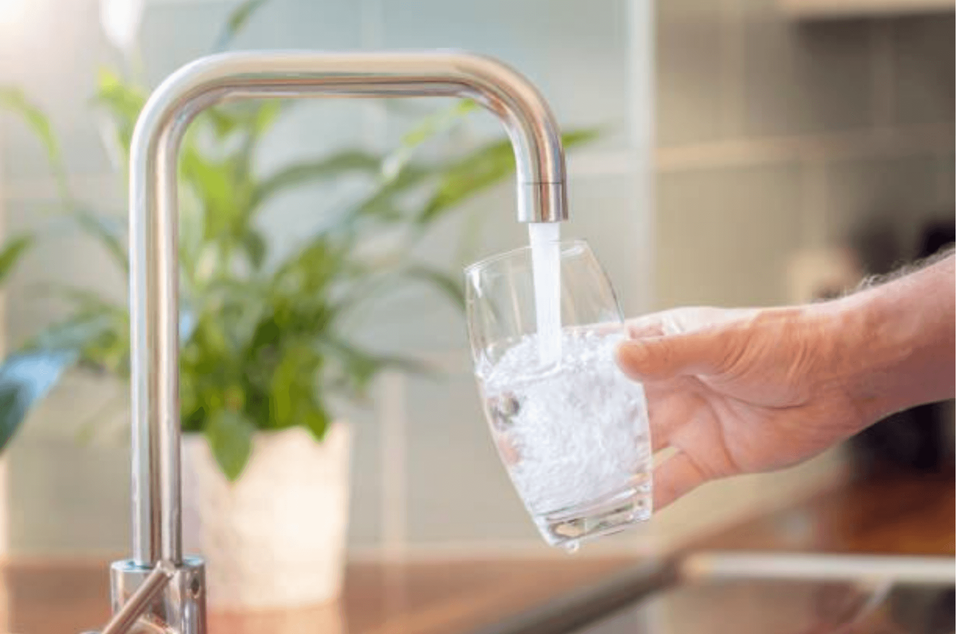 A hand holding a glass under a tap filling it with water.