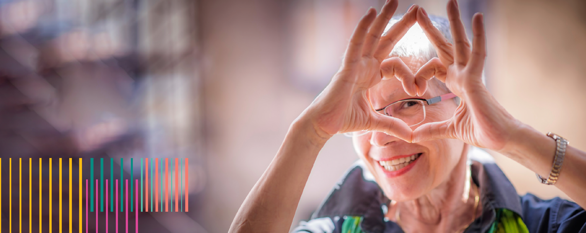 An older woman making a heart with her fingers smiling at the camera