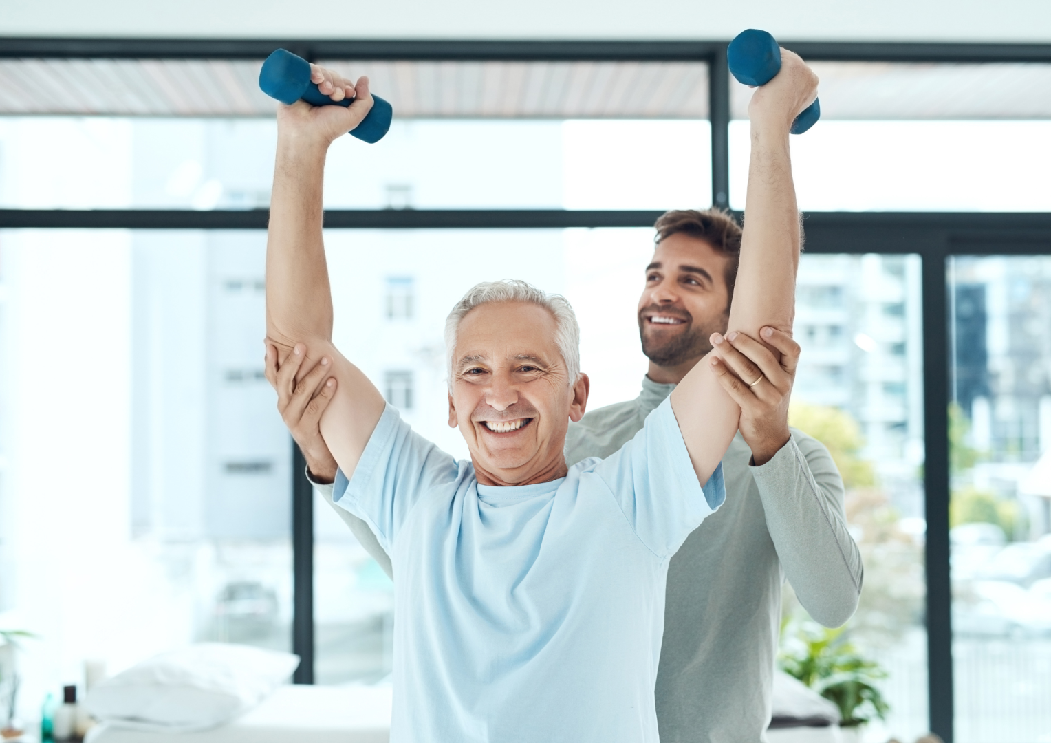 physiotherapist assists an elderly man to hold hand weights above his head.