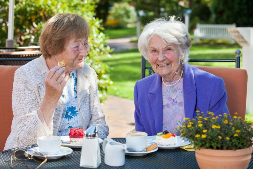two elder ladies having food outside on a sunny day, smiling